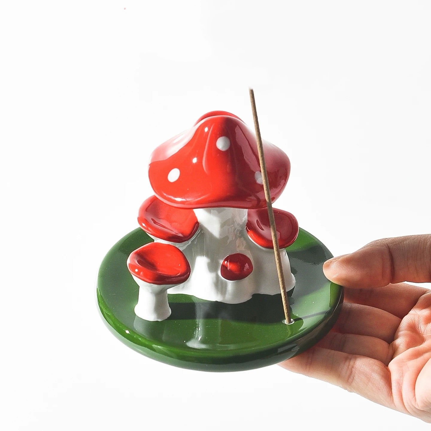 A hand holding the green base of the ceramic mushroom burner showing a stick incense inserted into the specific holder slot