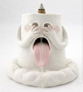 Handcrafted backflow incense burner smoke waterfall holder shaped like a blushing ghost with hands over its eyes, tongue out, and an incense cone on top against a white background