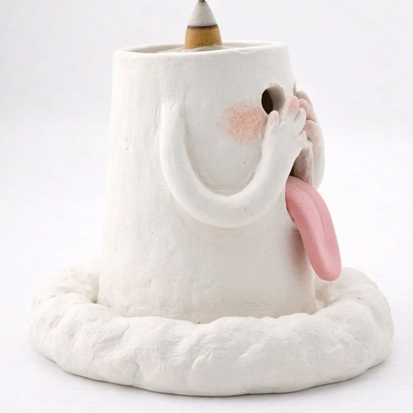 Rear side view of a handcrafted blushing ghost backflow incense burner with a pink tongue, raised arms, and an incense cone on top against a white background