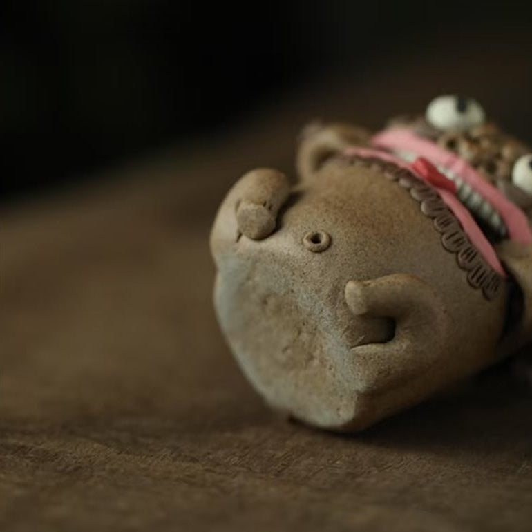 Bottom view of a handcrafted purple clay guardian backflow incense burner lying on its side, showing its circular base, small rounded feet, and central drainage hole on a wooden surface.