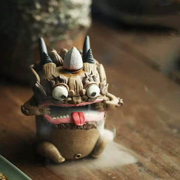 Full‑view of a handcrafted purple clay guardian backflow incense burner on a wooden table, with horns, bulging eyes, and white mist flowing from its mouth.
