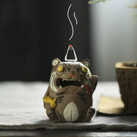 Handcrafted purple clay tiger guardian backflow incense burner displayed in use with a lit cone on top, showing curling smoke above the tiger figure in a warm tabletop setting.