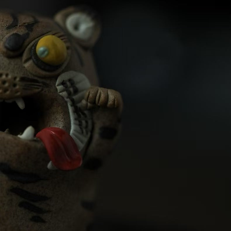 Close-up detail of the handcrafted purple clay tiger guardian incense burner, highlighting its bulging yellow eye, red tongue, raised paw, striped cheek, and textured handmade ceramic surface in a smoky dark setting.
