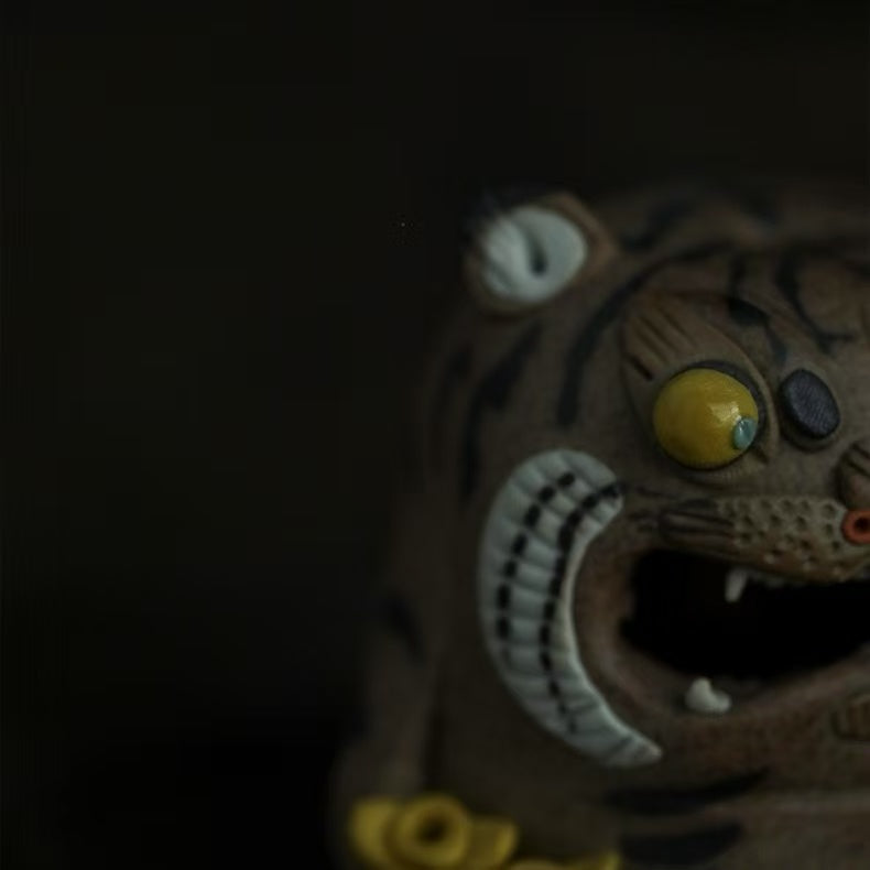 Side close-up of the handcrafted purple clay tiger guardian incense burner, showing its bulging yellow eye, striped face, open mouth, white fang detail, and textured purple clay body in a smoky low-light setting.