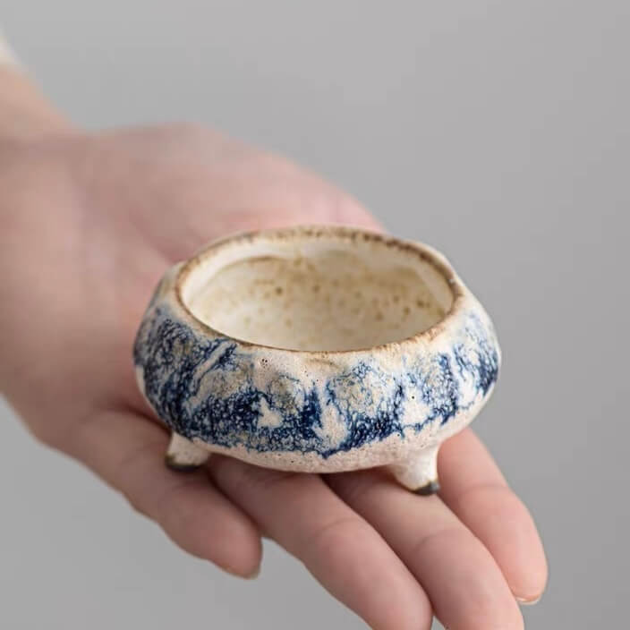 Hand holding a compact handmade blue marbled ceramic incense holder with a cream interior and three short feet