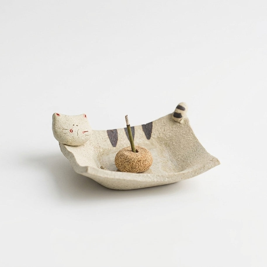 Handmade ceramic incense holder shaped like a curled cat, featuring a cream-colored dish with painted stripes, a small cat face and tail detail, and a central incense insert on a clean white background.