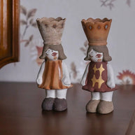 Two handmade ceramic girl incense burners with crown tops and patterned dresses standing on a wooden surface with a floral backdrop.