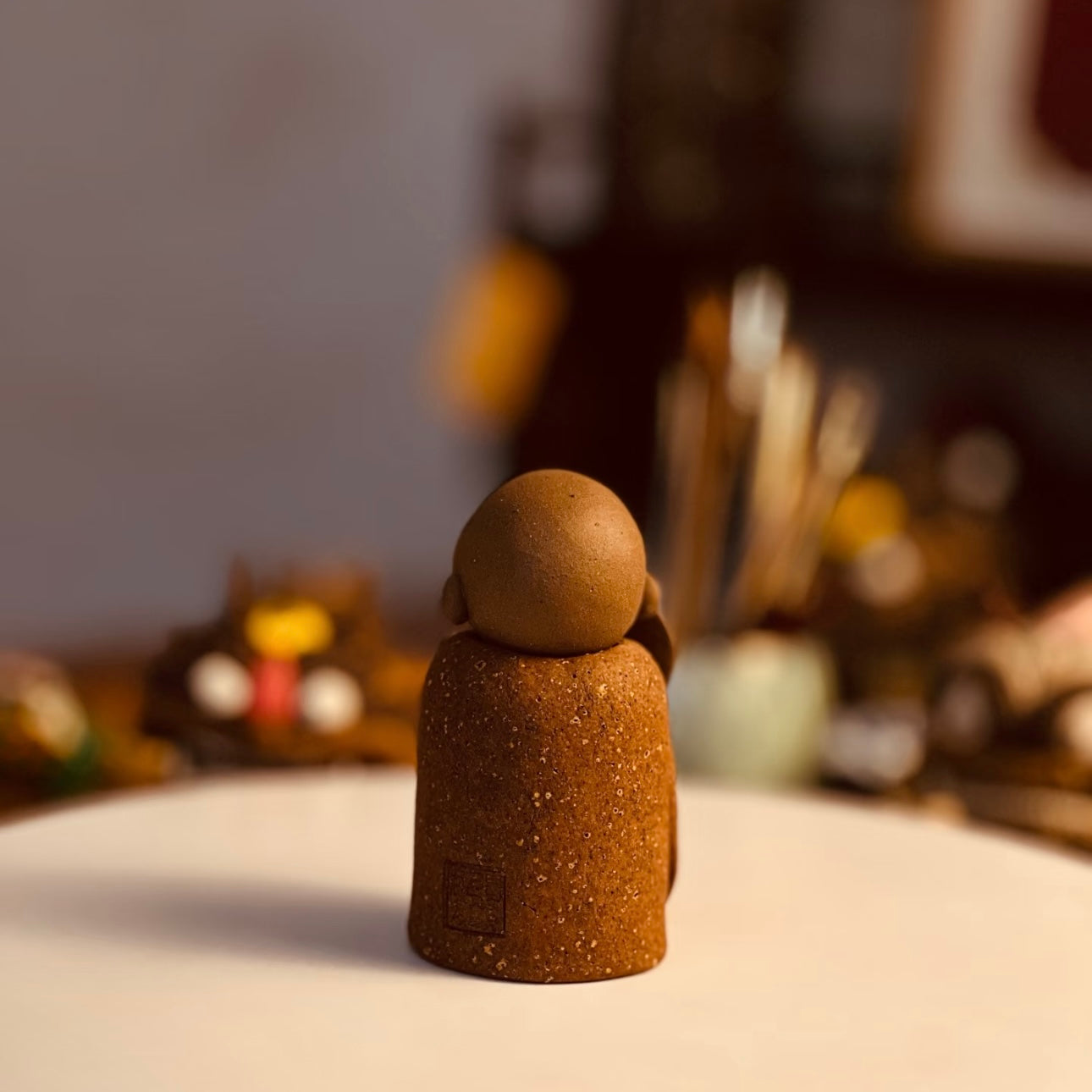 Rear view of The Joyful Little Monk handmade ceramic incense stick holder on a white tabletop in a warm softly blurred interior setting