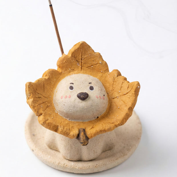 Handmade ceramic maple-leaf puppy incense holder with a cute puppy face framed by an autumn maple leaf collar, holding a stick incense on a round dish base against a white background.