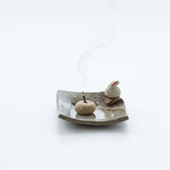 Handmade ceramic incense holder featuring a cute rabbit figurine, rustic square dish, and a lit incense stick with soft rising smoke, styled on a clean white background.