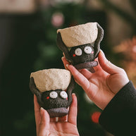 Two handmade ceramic Soot Spirit candle holders held in hands, showing their textured black bodies and cream tops.