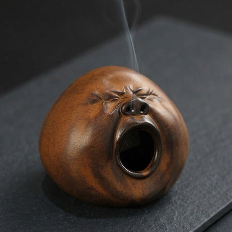 Handmade ceramic yawning face incense burner with smoke rising from the top