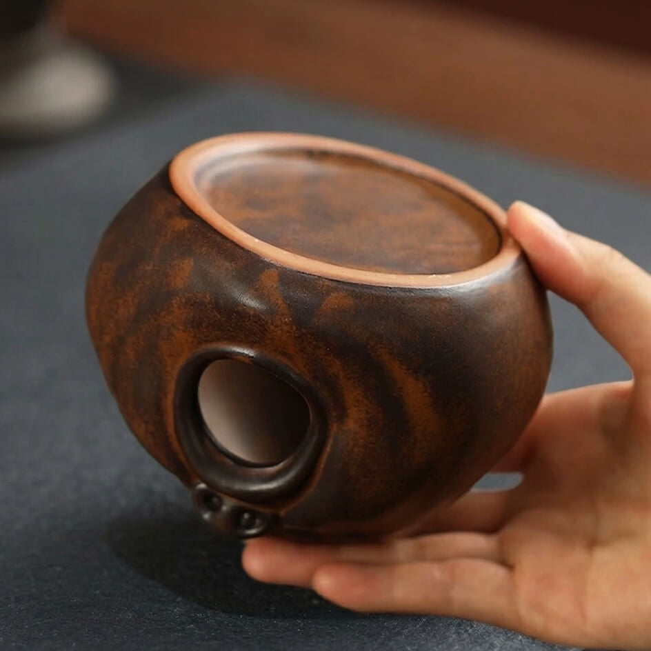 Back view of a handmade ceramic yawning face incense burner showing the top opening and hollow interior while held in hand