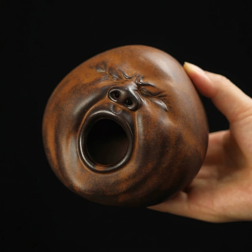 Close-up of a handmade ceramic yawning face incense burner held in hand