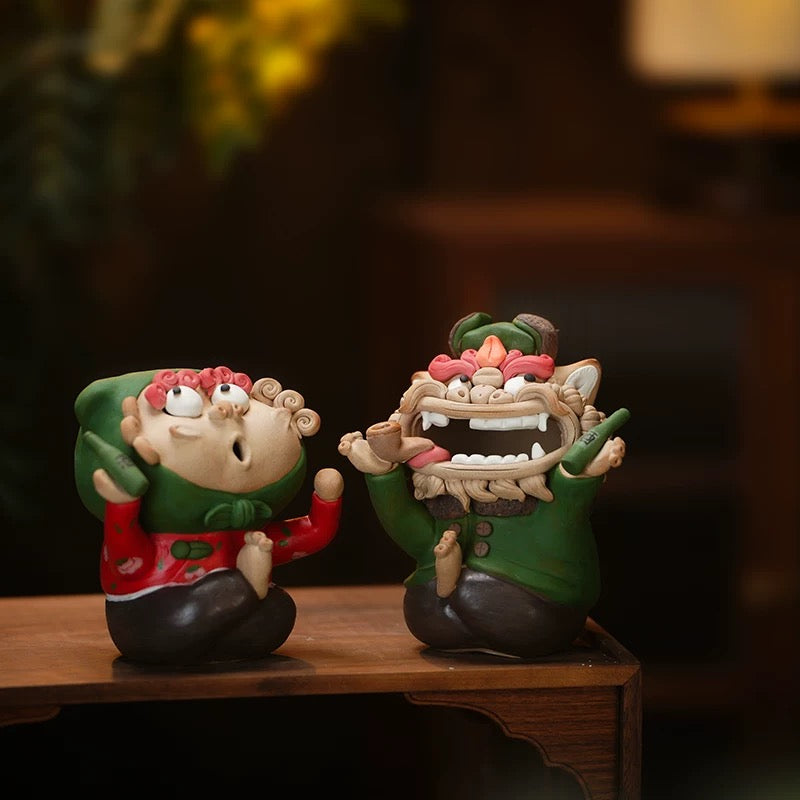 Handmade quirky ceramic incense holder duo featuring a green lion figure and a red figure displayed on a wooden table in a warm indoor setting