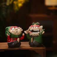 Handmade quirky ceramic incense holder duo featuring a green lion figure and a red figure displayed on a wooden table in a warm indoor setting
