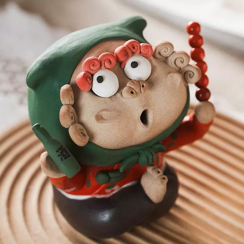  Handmade quirky ceramic incense holder shaped like a red figure holding a bottle and skewer, displayed on a textured tray in a warm indoor setting