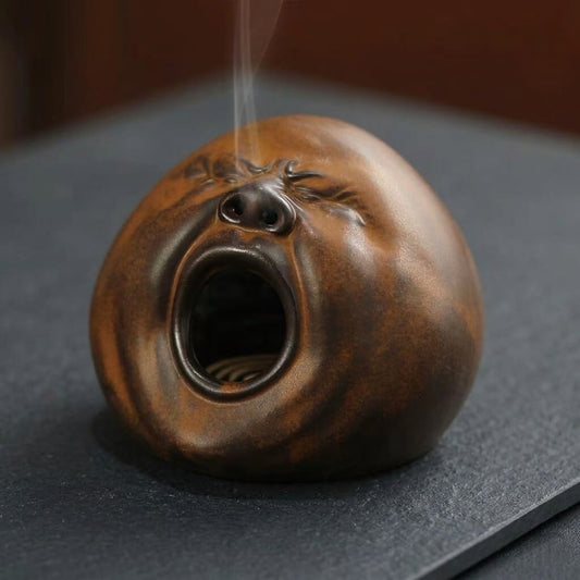 Handmade yawning face incense burner with rounded ceramic design and smoke rising from the top