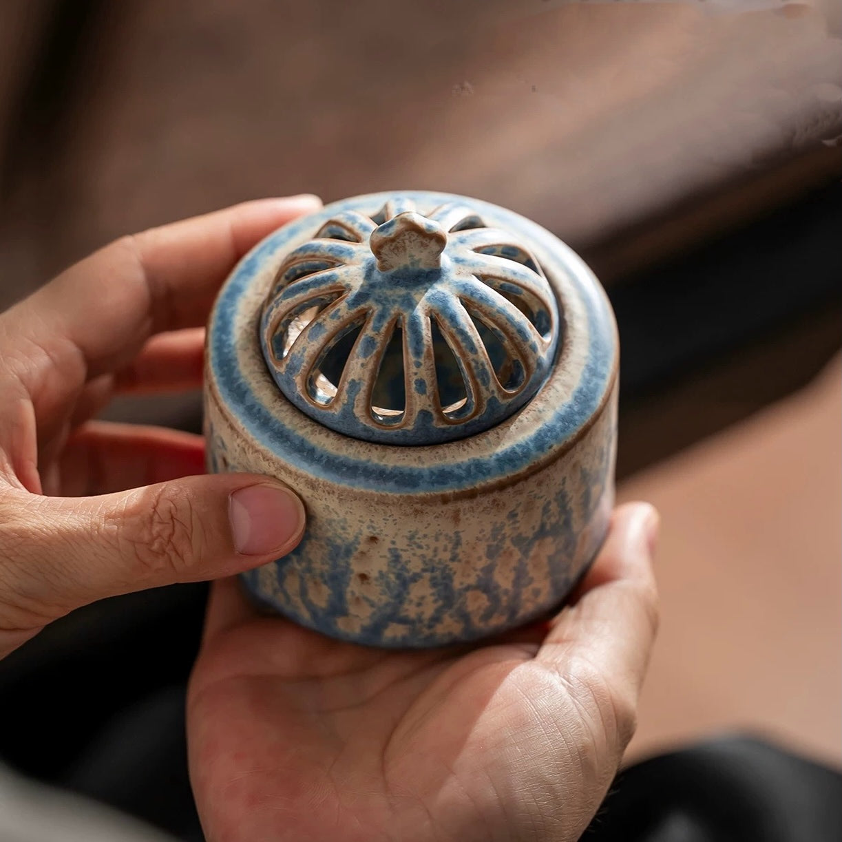 Compact handmade ceramic electric incense burner in blue glaze held in two hands to show small palm size.