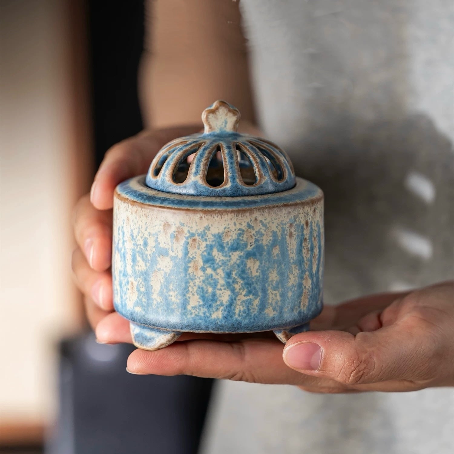 Handmade blue ceramic electric incense burner with vented lid held in two hands to show size and design.