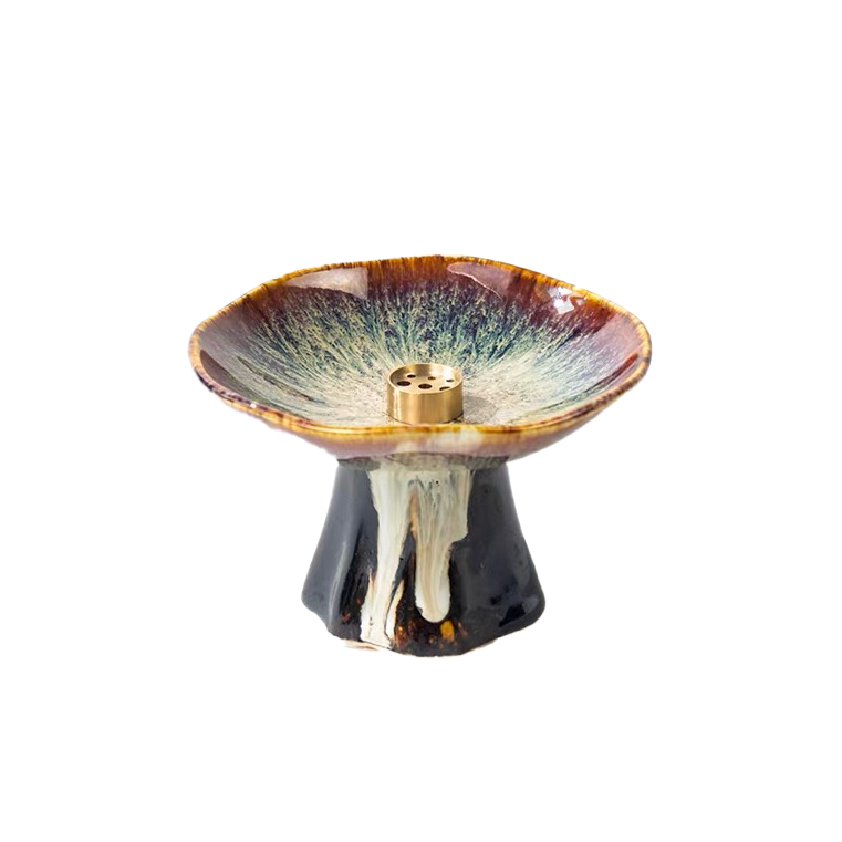 Japanese minimalist ceramic incense holder with a pedestal base, shallow glazed dish, and brass incense insert, featuring earthy brown, cream, and black tones on a clean white background.
