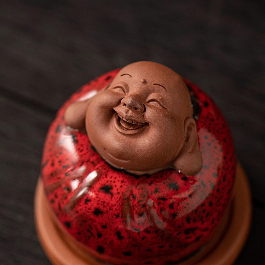 Close up view of the smiling face and glossy red speckled finish on a laughing Buddha incense burner