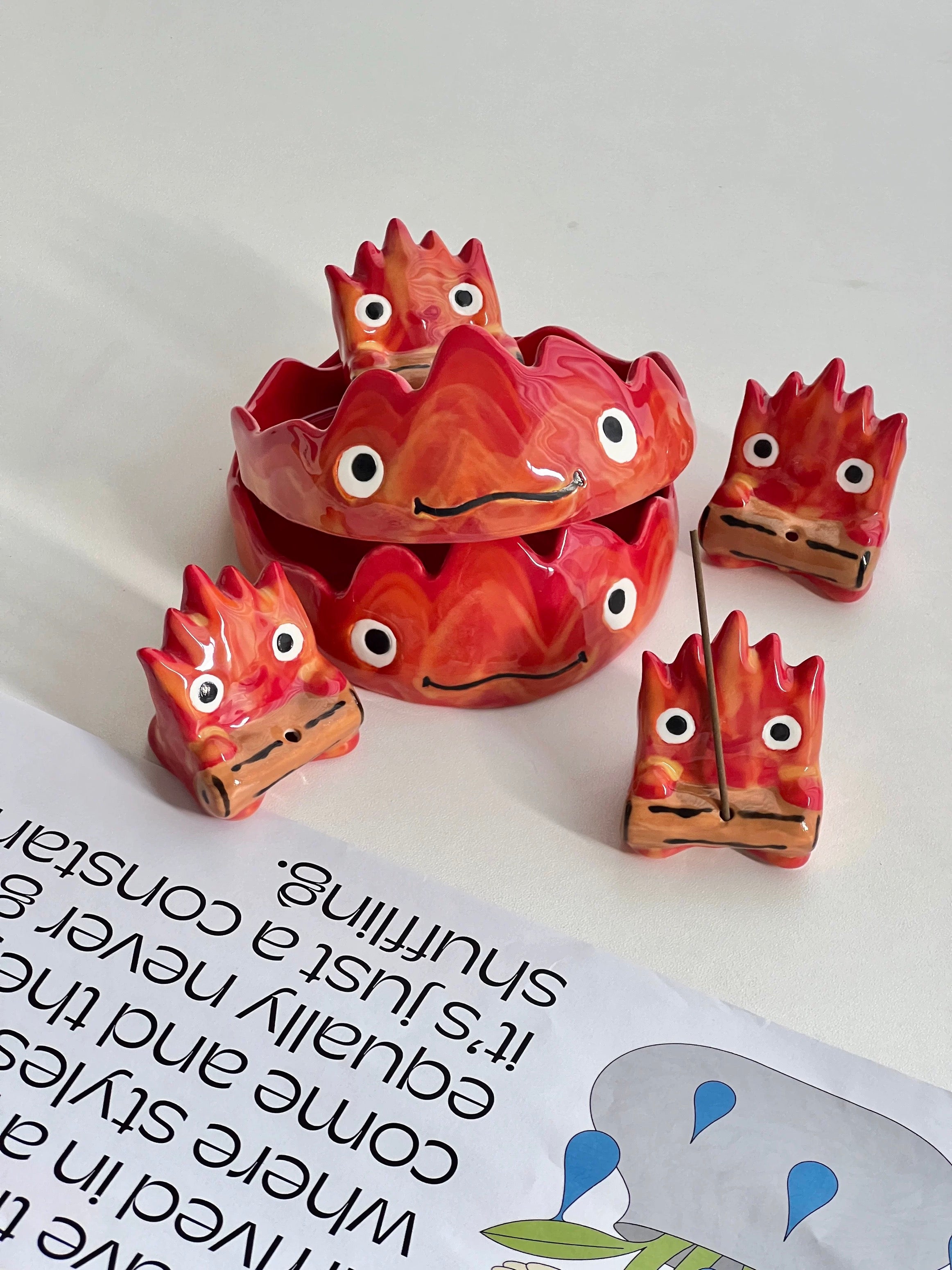 Group shot of red flame character incense holders with stacked trays and four small holders on a white surface with a magazine page.