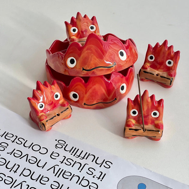 Group shot of red flame character incense holders with stacked trays and four small holders on a white surface with a magazine page.