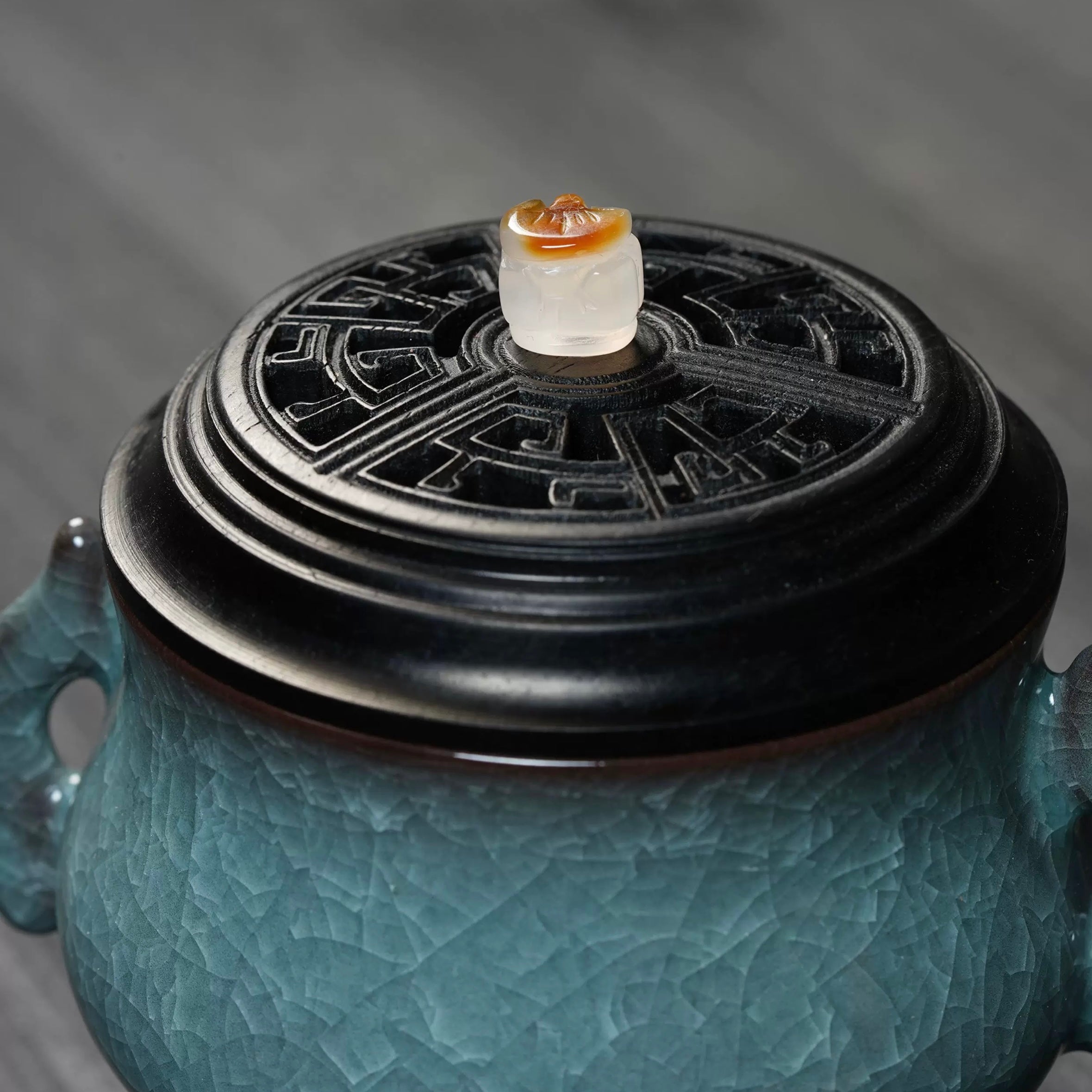 Close-up of a luxury electric incense burner with a Ge kiln ice-crackle ceramic body, carved black lid, and side handles