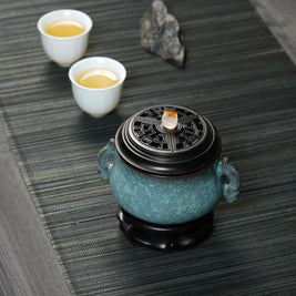 Luxury electric incense burner on a tea table with two teacups, featuring a Ge kiln ice-crackle ceramic body, black lid, and decorative base