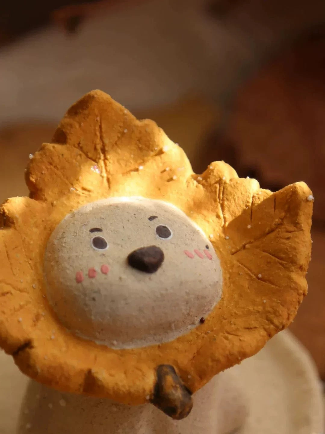 Close-up of the ceramic puppy incense holder with a yellow maple leaf ruff, face details in focus against a warm autumn background.
