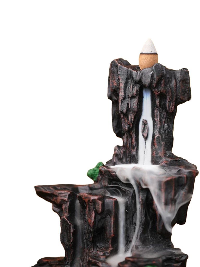 Front angled view of a mountain-style backflow incense burner with a cone placed at the top, showing white smoke flowing down the dark rocky tiers like a waterfall, with a small green moss accent on a white background.