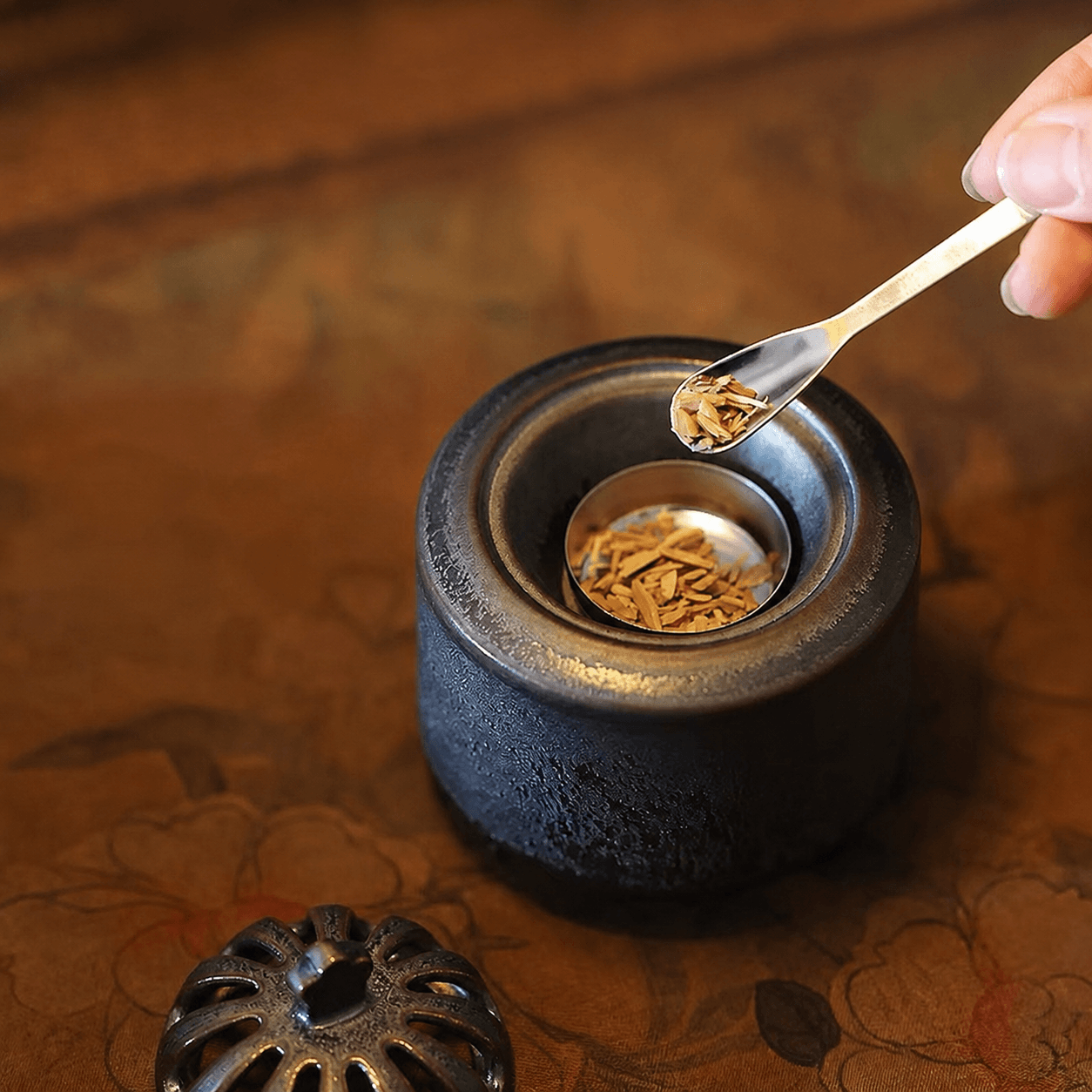 Obsidian black ceramic electric incense burner with the lid removed while incense wood chips are added to the metal heating dish