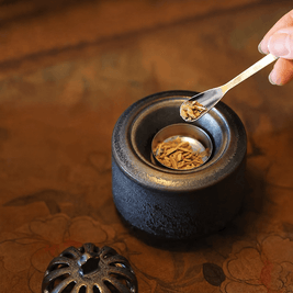 Obsidian black ceramic electric incense burner with the lid removed while incense wood chips are added to the metal heating dish