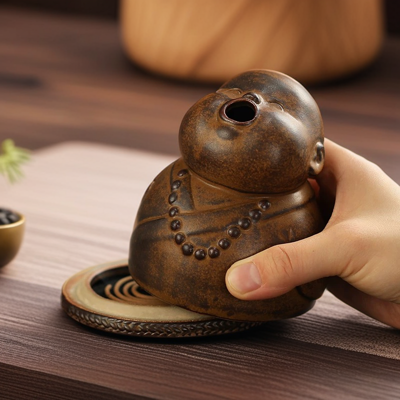 A hand lifting the brown ceramic peaceful little monk incense burner to reveal a spiral incense coil resting on the base, demonstrating the internal design and how to place the aromatherapy incense.