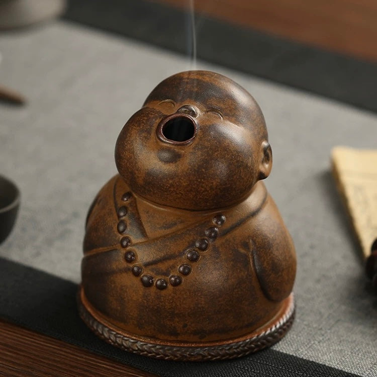 Front view of the Peaceful Little Monk Incense Burner, showing the rounded monk figure with a smoke outlet at the mouth, brown ceramic finish, and prayer bead decoration.