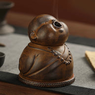 Side view of the Peaceful Little Monk Incense Burner, showing the monk’s rounded face, upward smoke outlet, brown ceramic texture, and prayer bead details.