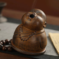 Close-up of the Peaceful Little Monk Incense Burner showing the smoke outlet on the monk’s mouth, brown ceramic finish, prayer bead details, and rounded monk figure design.
