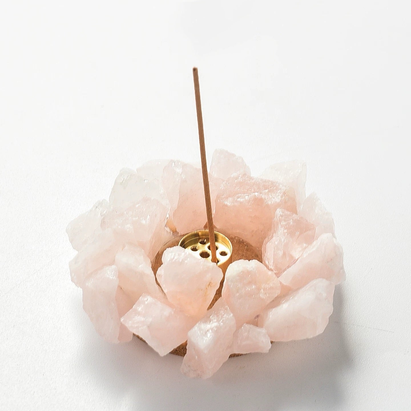 Raw pink rose quartz crystal incense holder with brass insert holding an incense stick on white background