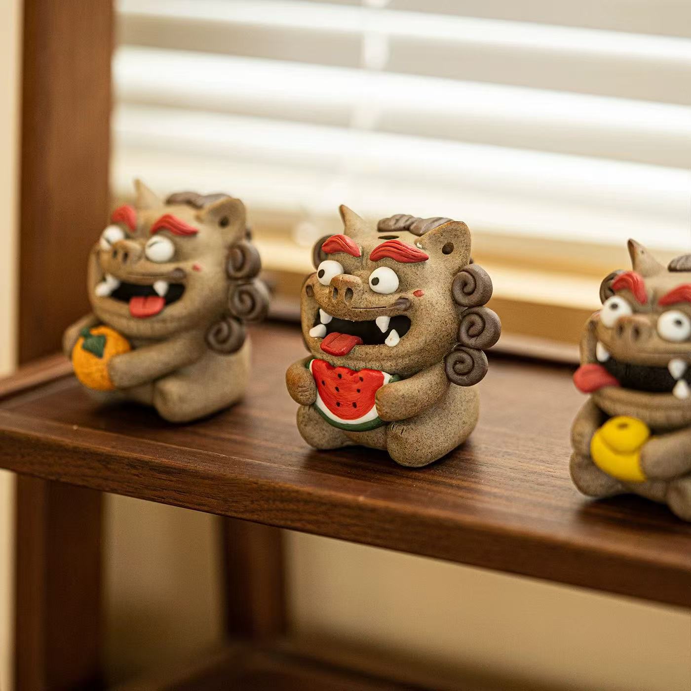 A lineup of four Pixiu backflow incense burners on a black tray, with the front‑right figure clutching a watermelon slice in clear focus, its open mouth emitting a mist‑like cascade, and three other Pixiu figures softly blurred behind.