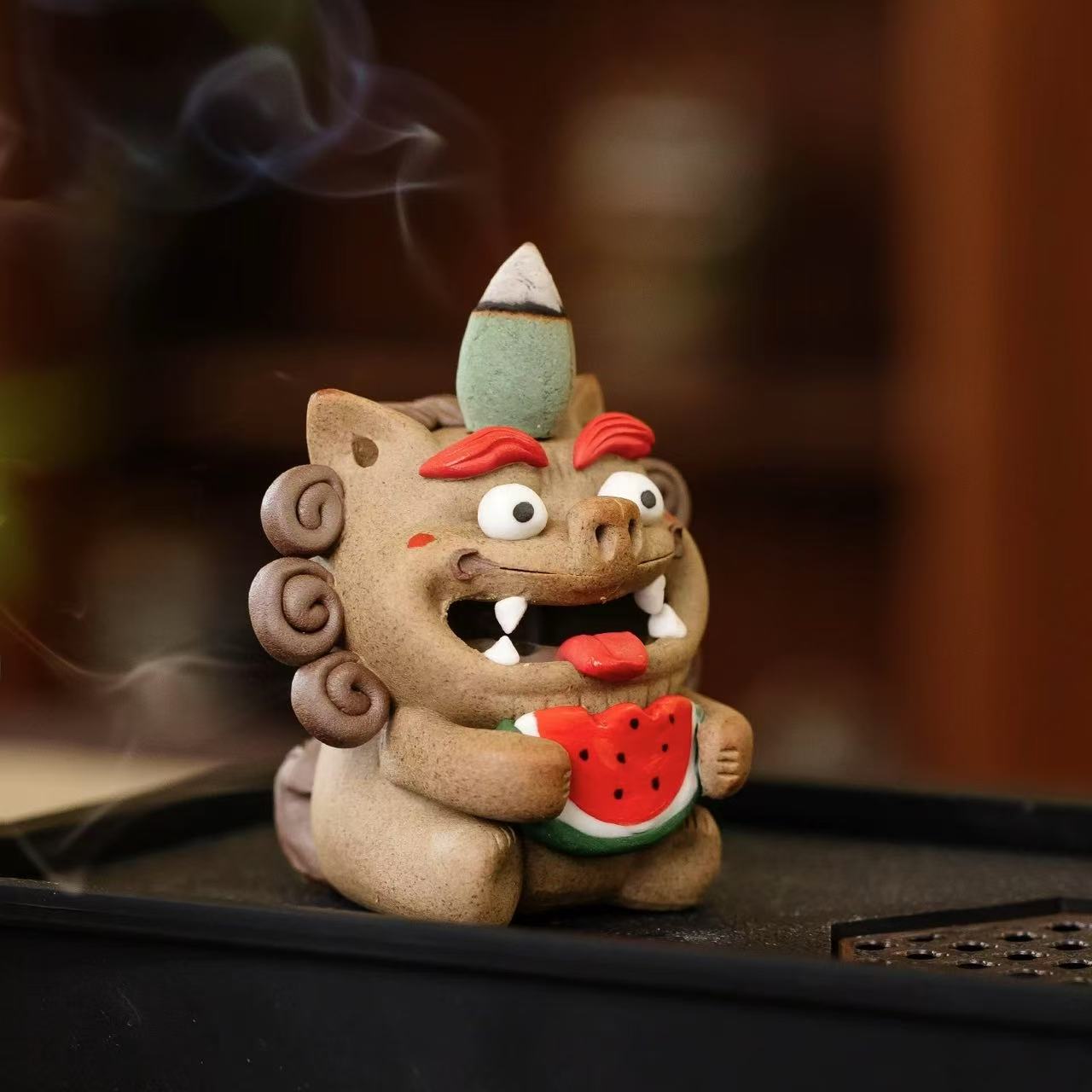Hand‑crafted ceramic Pixiu incense burner holding a bright watermelon slice on a black tray, topped with a lit backflow cone on its head and emitting a gentle smoke waterfall from its open mouth.