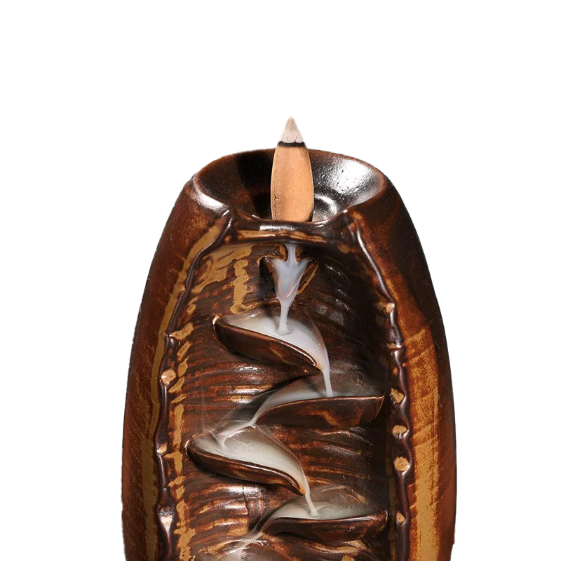 Close-up of a premium high-fired ceramic backflow incense holder in a rustic brown glaze with an incense cone and cascading smoke flow against a white background