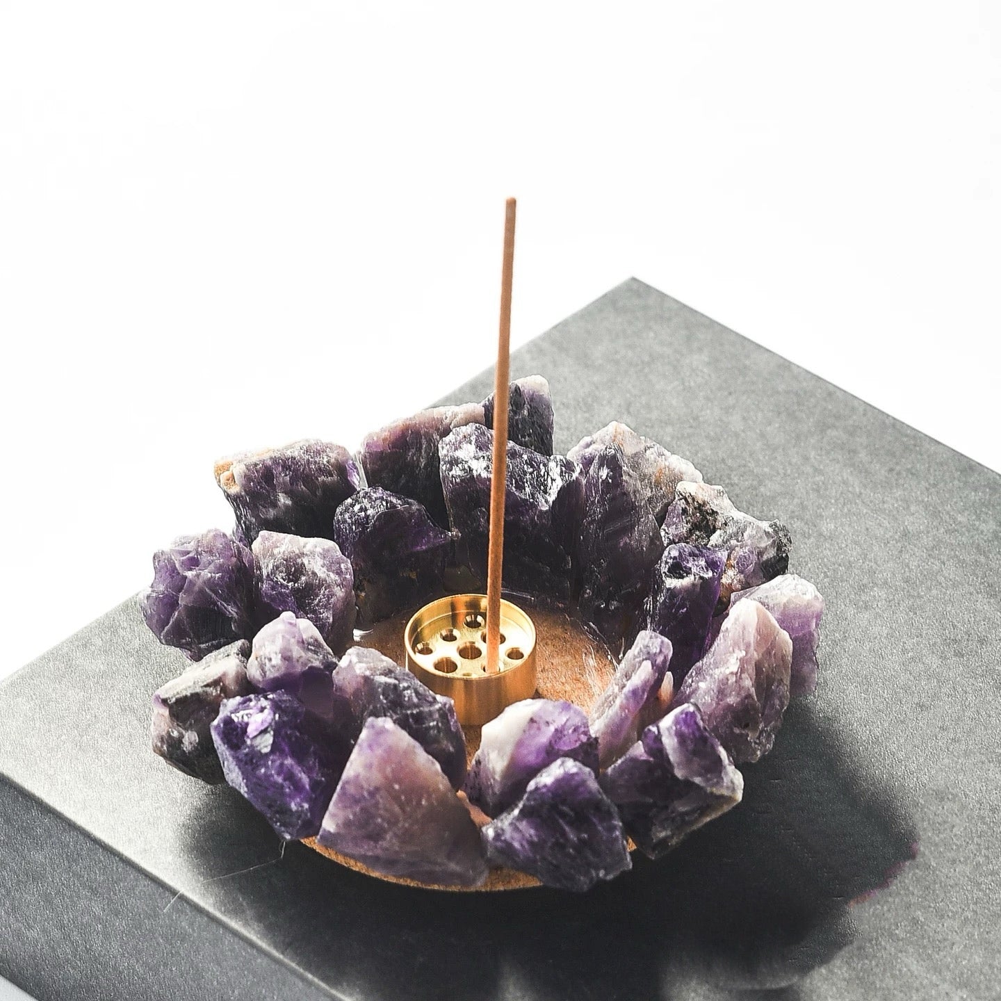 Raw purple amethyst crystal incense holder with brass insert styled on a black stone base with incense stick