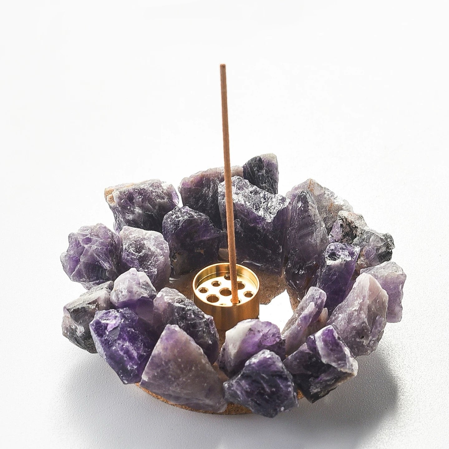 Raw purple amethyst crystal incense holder with brass insert holding an incense stick on white background