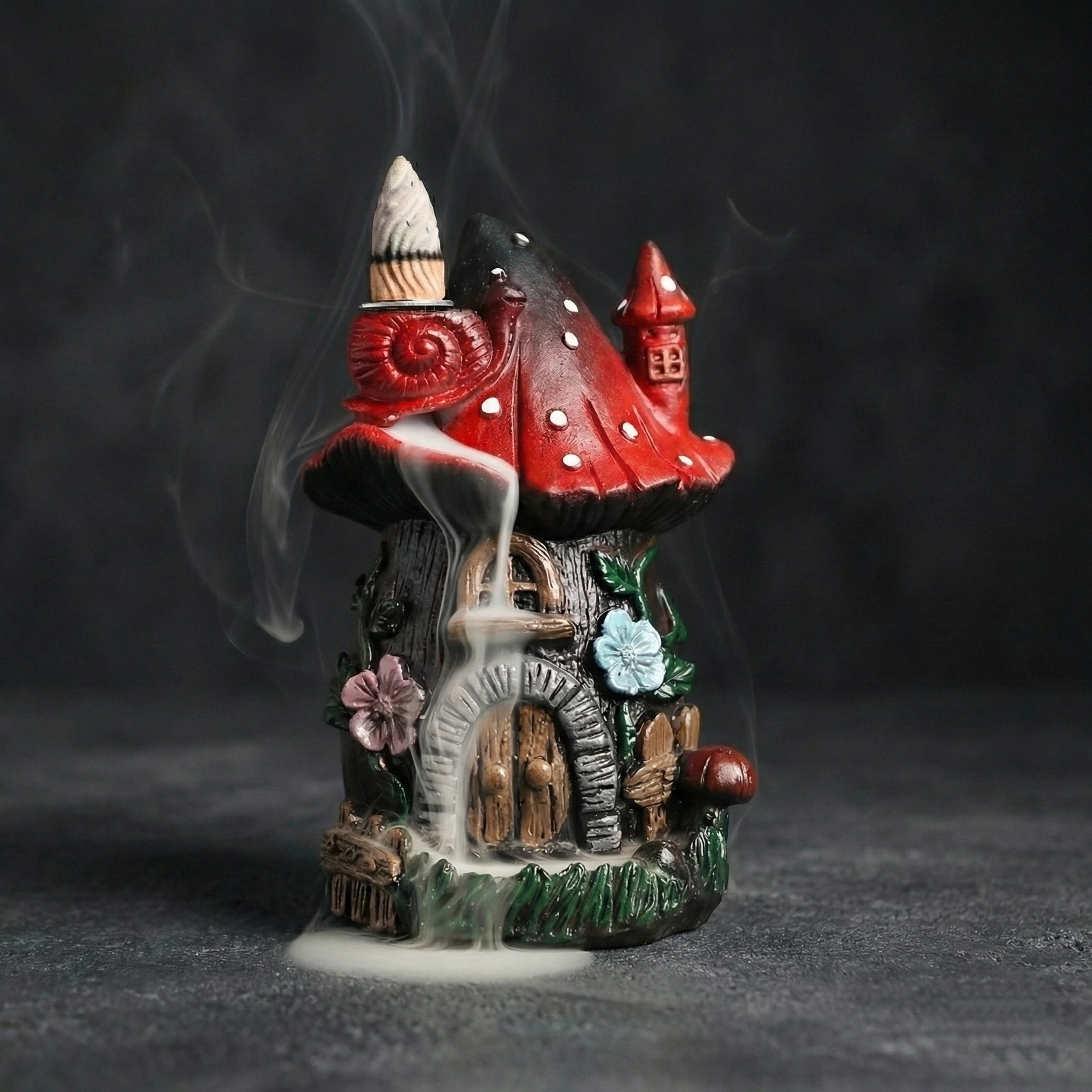 Resin mushroom backflow incense burner shaped like a red mushroom house with cascading smoke, floral details, and a fairy cottage design on a dark background