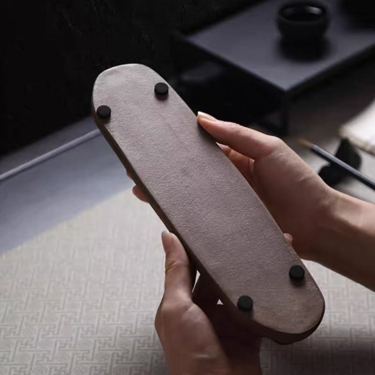 Bottom view of a rustic ceramic incense holder box with anti-slip feet, held in hands to show its textured base.