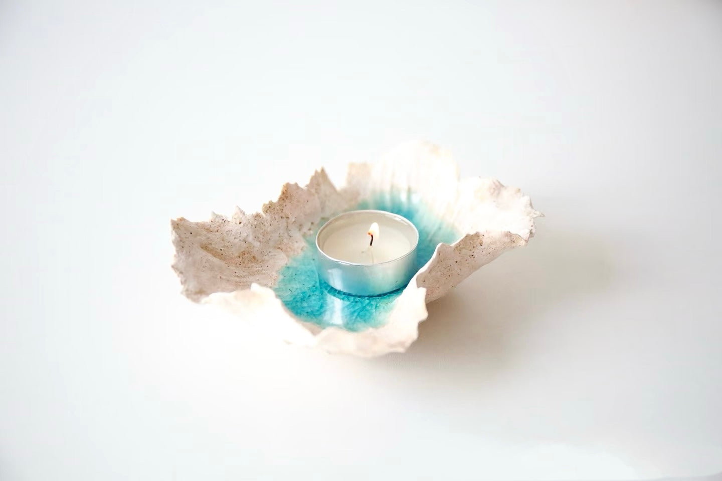 Sea Blossom handmade ceramic incense and candle holder with an organic sculpted rim and ocean blue glaze center, displayed with a tealight candle on a clean white background