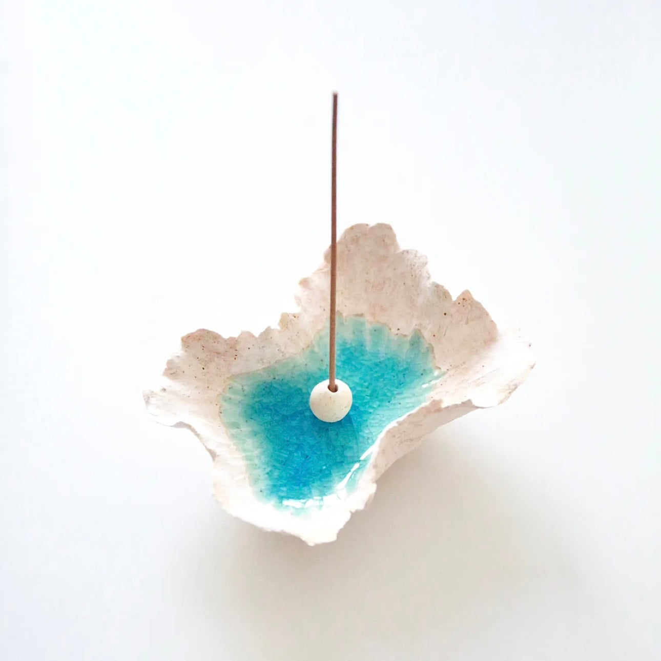 Sea Blossom handmade ceramic incense and candle holder with a blue lagoon glaze center, shown holding an incense stick with a white ceramic bead on a clean white background