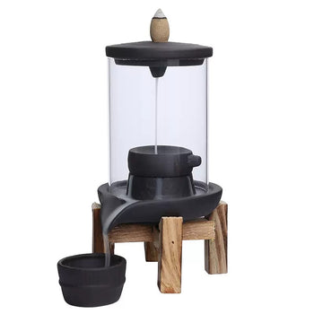 Clear-dome backflow incense burner with a black ceramic lid and base, wooden stand, and separate ash cup, topped with a cone incense on a white background.