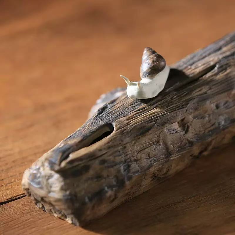 Close-up of a snail-inspired ceramic incense holder box with a small snail ornament on a textured tree branch lid.